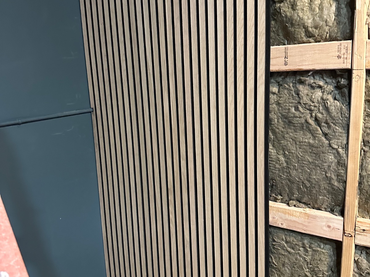 Panagraph Studios build — the first slat panel fixed beside the exposed mineral wool it covers