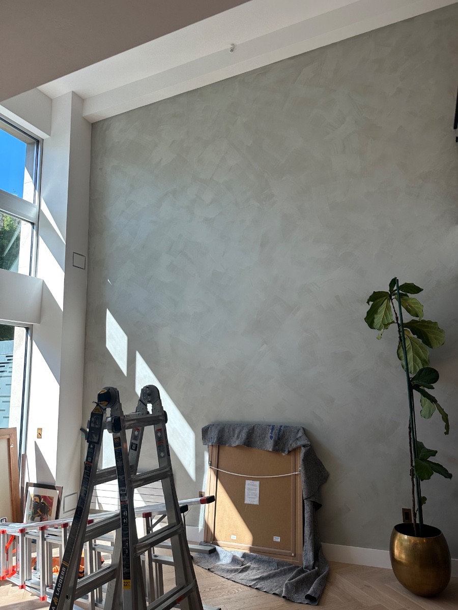 Russian Hill gallery wall — the bare double-height plaster wall before installation, with the first wrapped work waiting