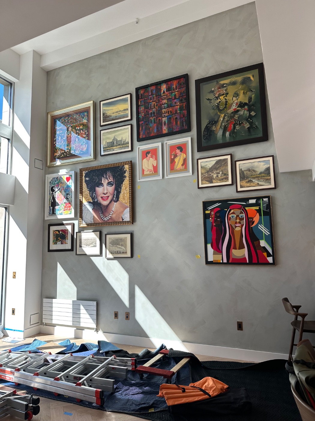 A double-height gallery wall of framed works on polished plaster in a Russian Hill residence, San Francisco, during installation