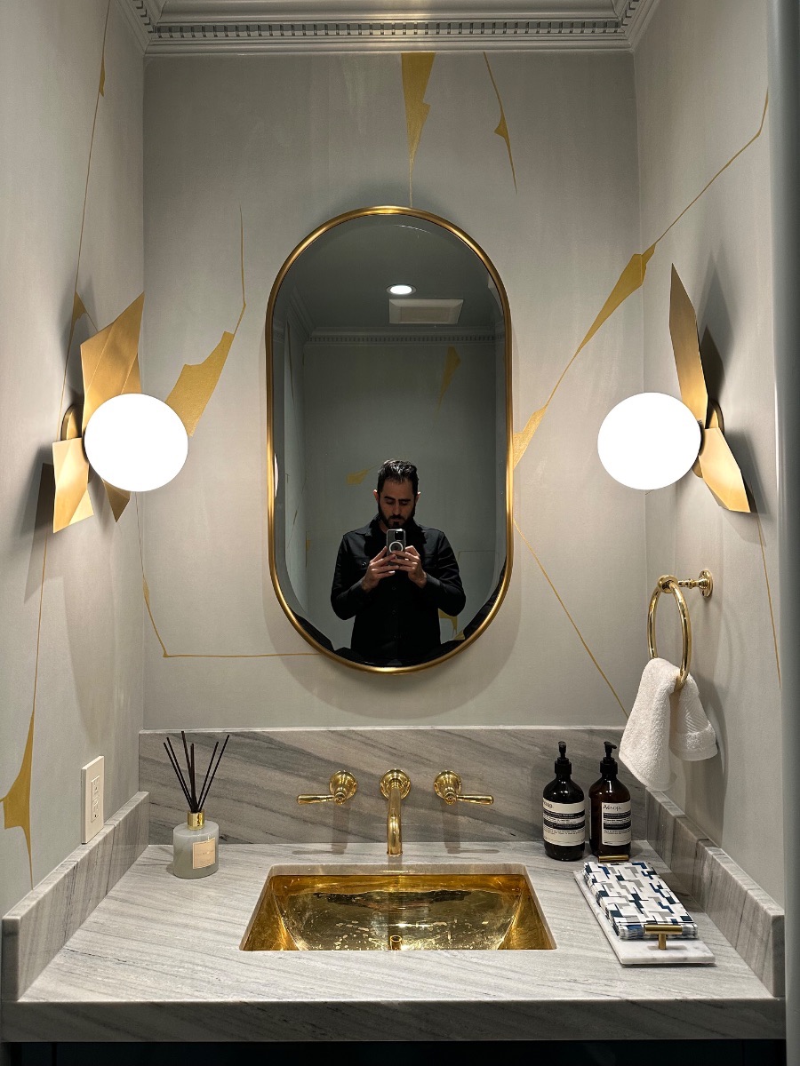 Fine art installation by Aero Luxe &mdash; An oval mirror and pair of sconces set above a marble vanity, Beverly Hills, California