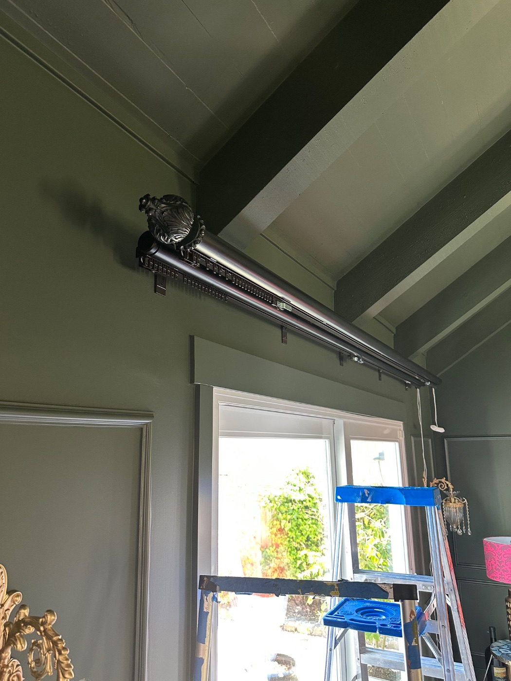 A traverse rod with an ornate finial and concealed carrier track set above a window casing