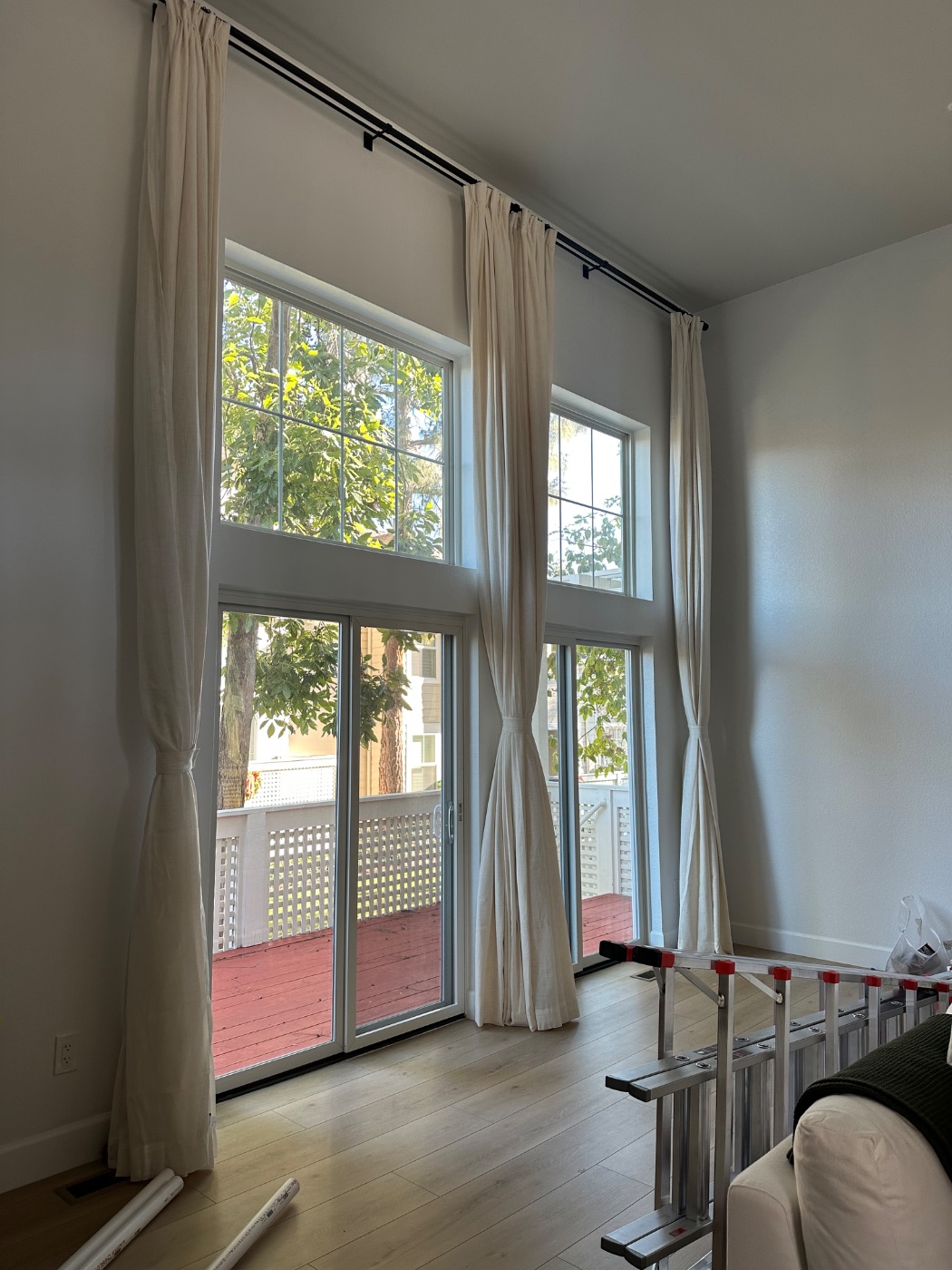 Full-length linen drapery on black iron rods across double-height windows and a sliding door, installed by Aero Luxe
